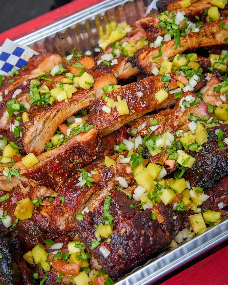 A tray of glazed baby back ribs topped with pineapple, onion and cilantro