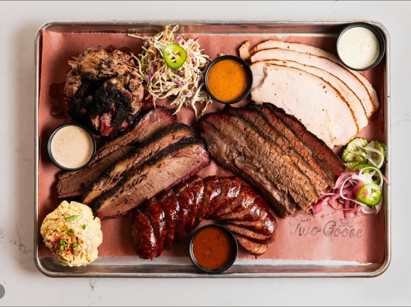 A full BBQ tray: brisket, turkey, sausage, sides, sauces on butcher paper