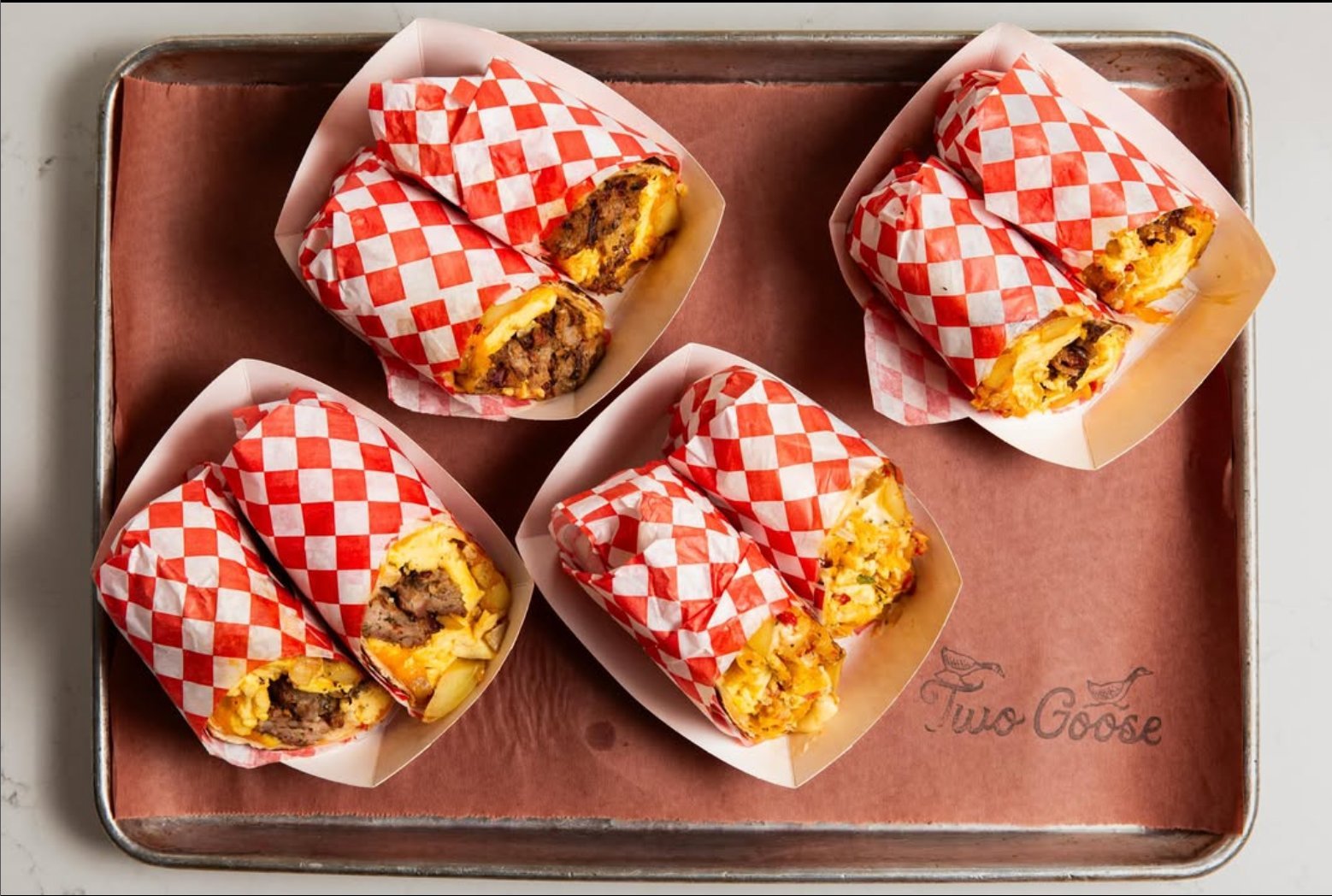 Four brisket breakfast burritos in red checkered wrappers on a Two Goose tray