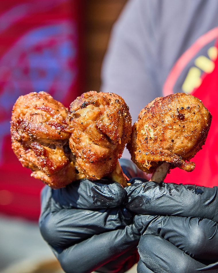 Three seasoned chicken lollipops held up in a gloved hand