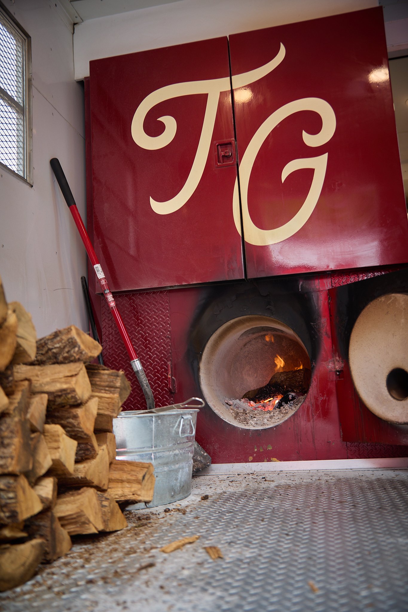 The Two Goose smoker doors with TG monogram, oak burning in the firebox